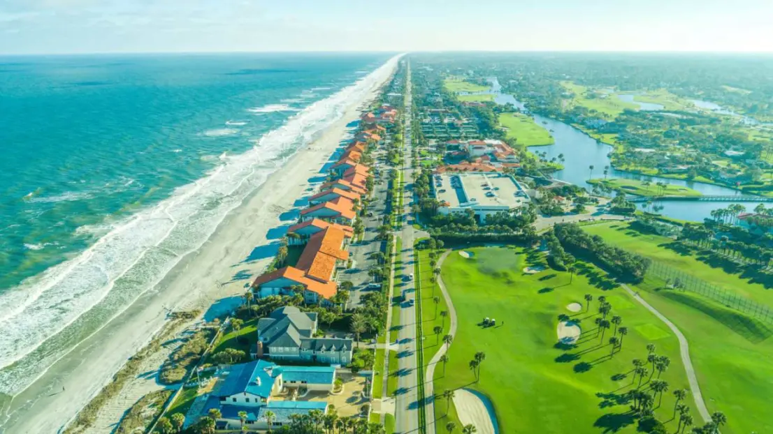 A bird’s-eye view of Ponte Vedra Beach in Jacksonville, FL, featuring the ocean, a golf course, forests, and a river.