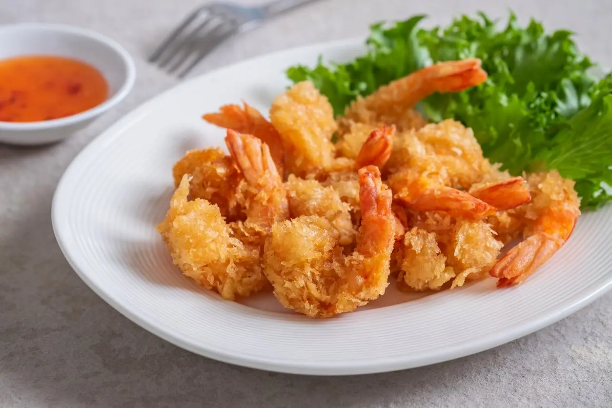 A plate of fried shrimp with lettuce and cocktail sauce. 