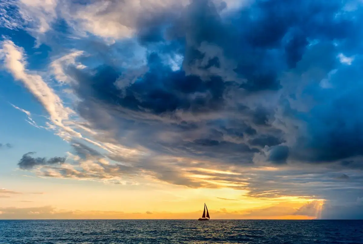 Storm clouds looming over a sailboat at sea.