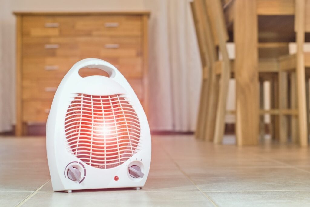 A portable electric fan heater sits on the tile floor of a home.