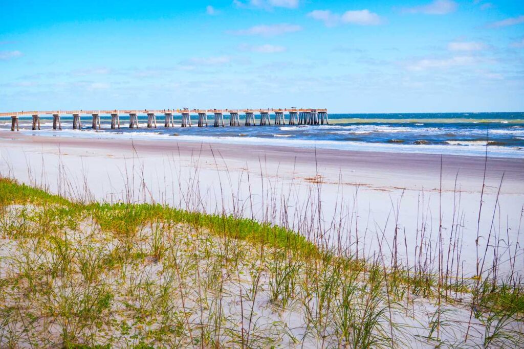 The Jacksonville Fishing Pier, as seen from a grassy dune on a sunny day.