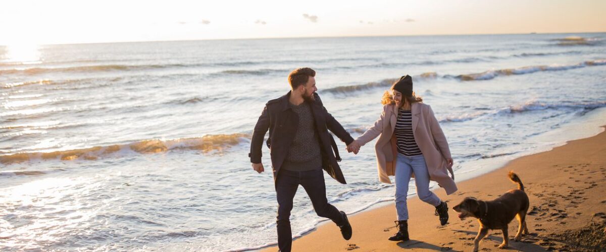 Couple at the beach in the winter with their dog.