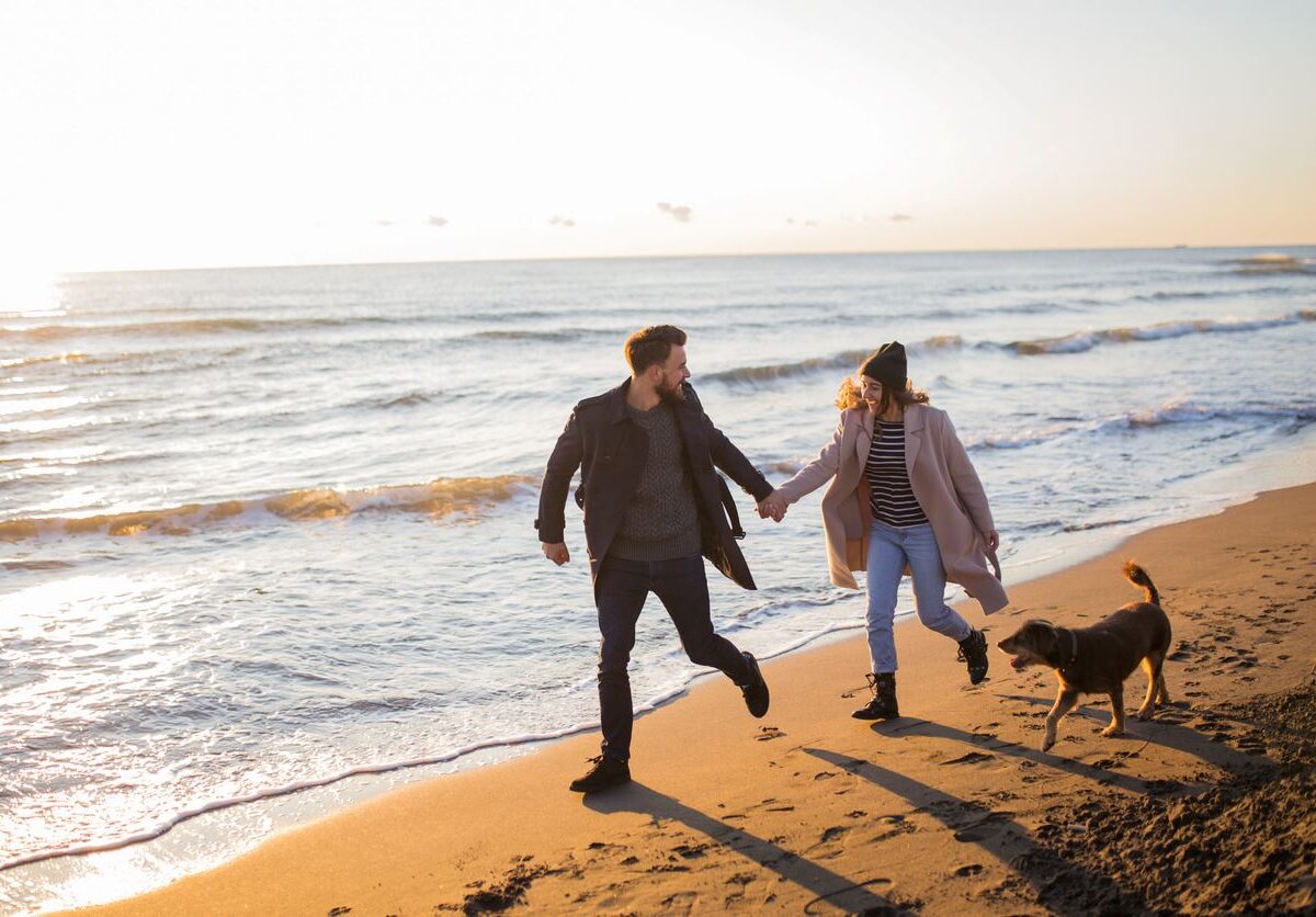 Couple at the beach in the winter with their dog.