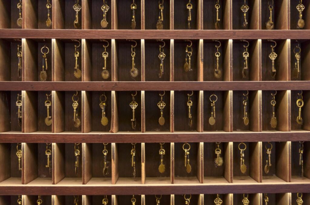 An array of vintage hotel keys on hooks within wooden shelving.