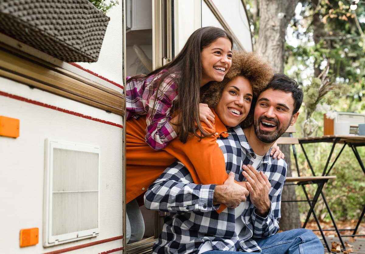 A family enjoying time together outside their RV during a camping trip, smiling and looking out the door.