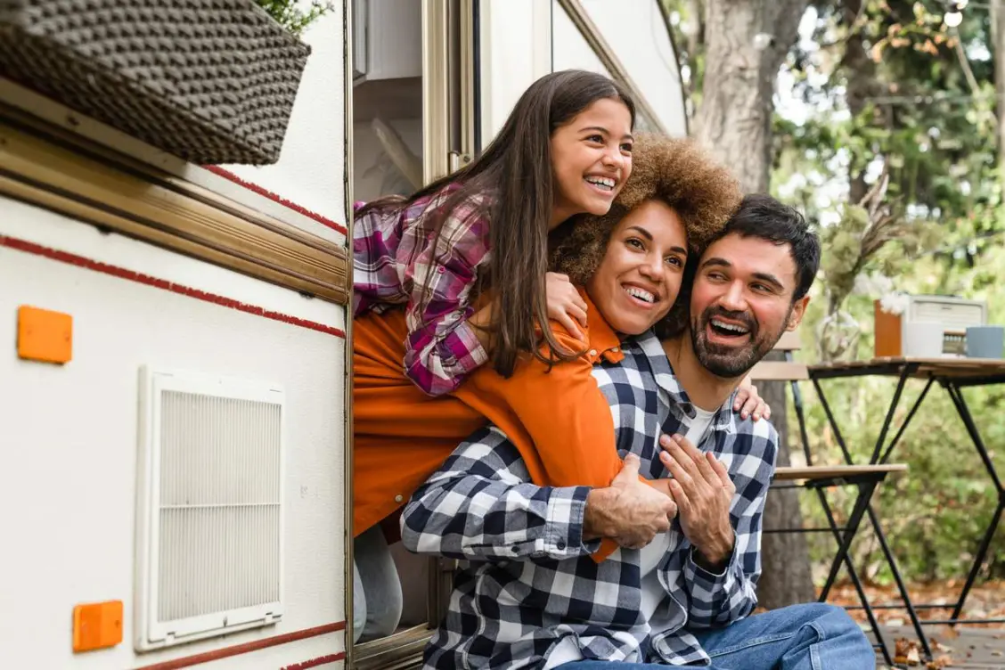 A family enjoying time together outside their RV during a camping trip, smiling and looking out the door.