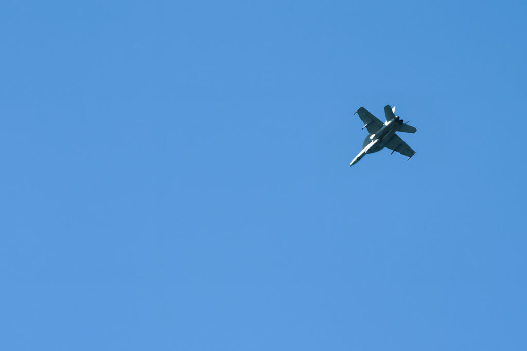 Prominent in military aviation, the F/A-18 Hornet, representing the US Navy's aerial might, soars effortlessly, showcasing its engineering and aerodynamic capabilities against a serene blue backdrop.