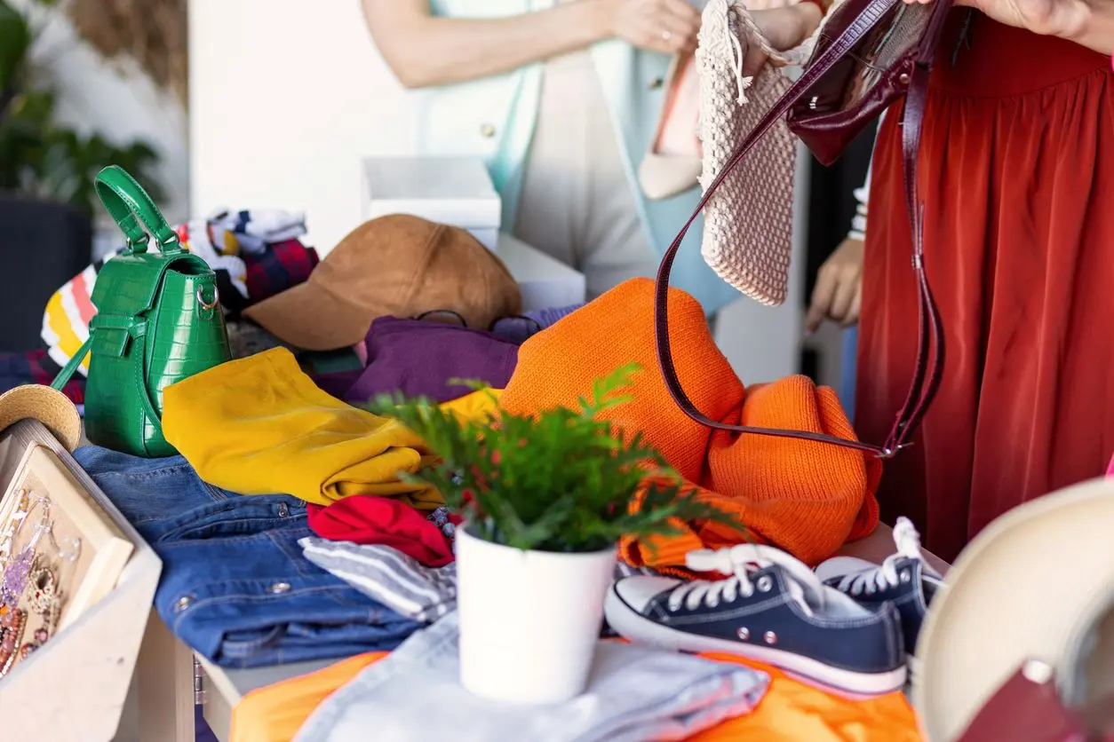 A table covered with colorful clothes, shoes, bags, and accessories, with people organizing them. 