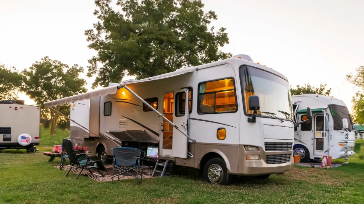 An RV parked at a campsite with chairs and tables set up outside under the awning.