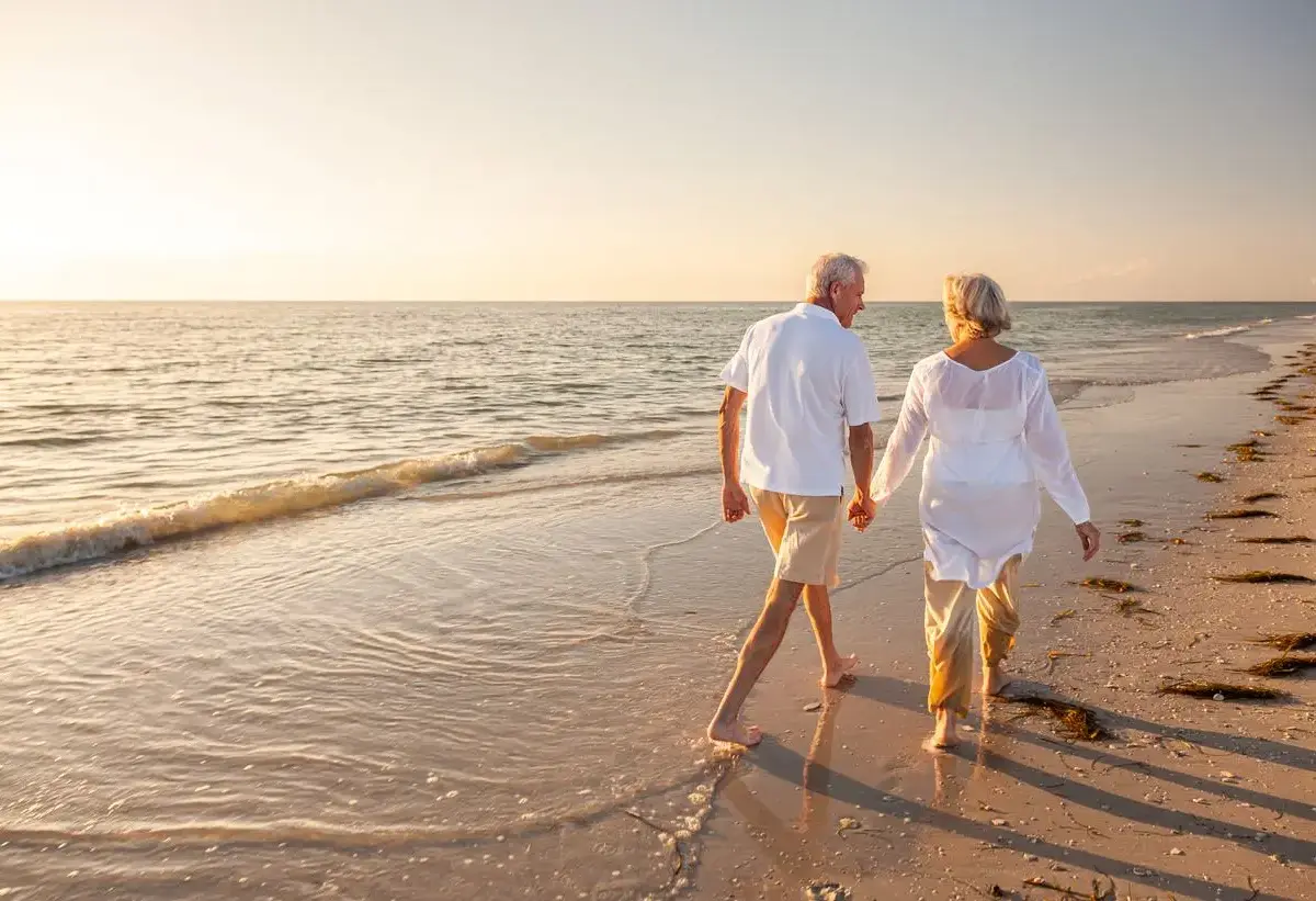 Happy senior man and woman old retired couple walking and holding hands on a beach at sunset