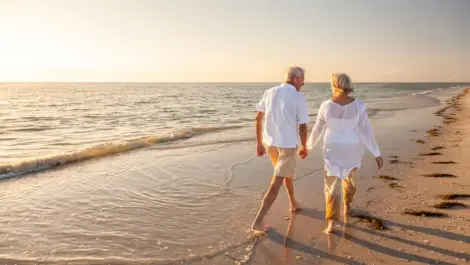 Happy senior man and woman old retired couple walking and holding hands on a beach at sunset